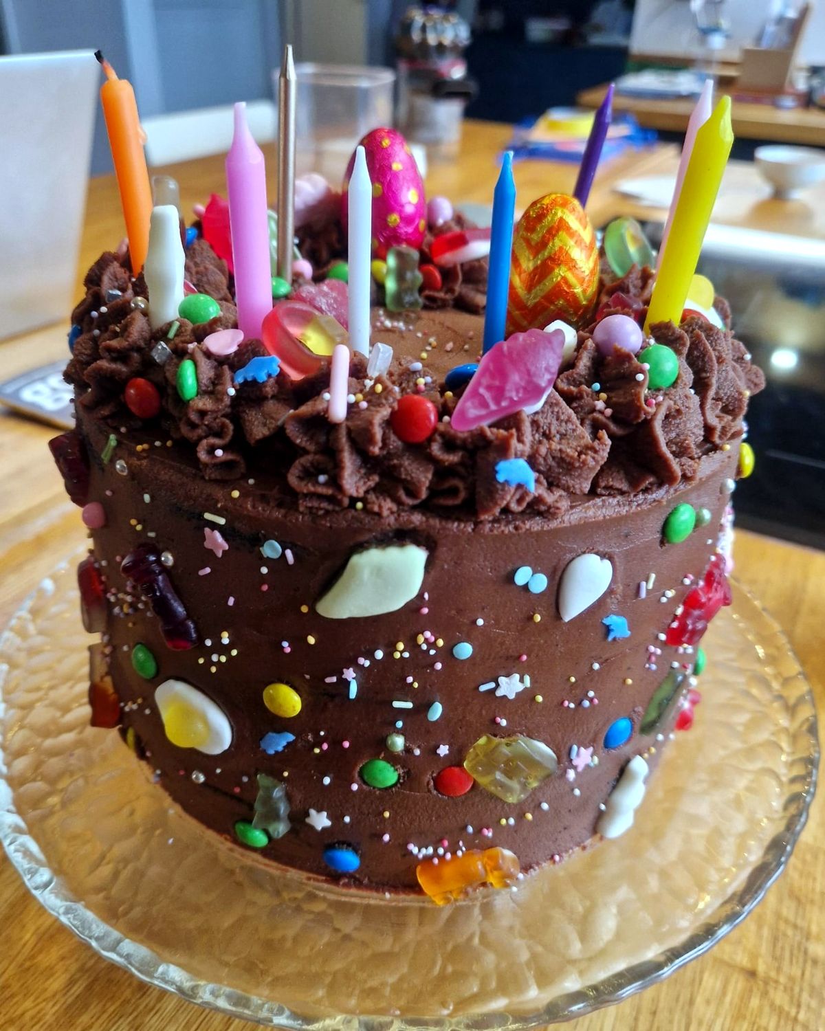 Chocolate birthday cake covered in sweets, sprinkles and candles